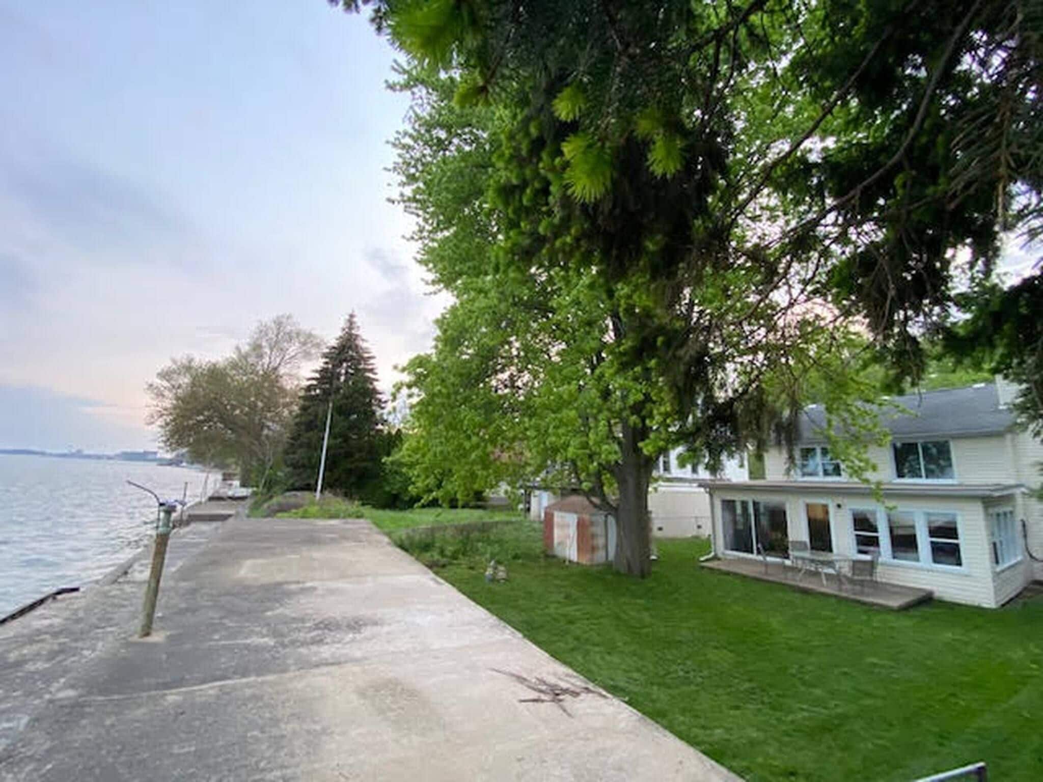 A waterfront property with a grassy area, a concrete pathway, and a house with a covered porch.