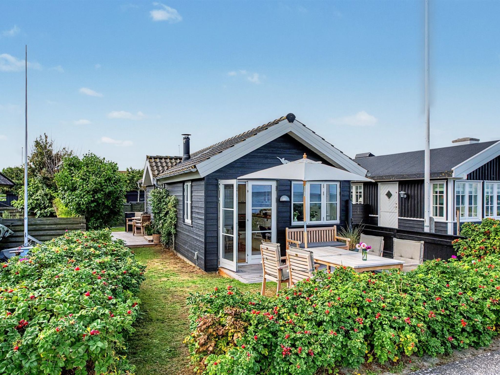 Una casa moderna con un amplio ventanal, un patio con mobiliario exterior y un jardín cuidado.