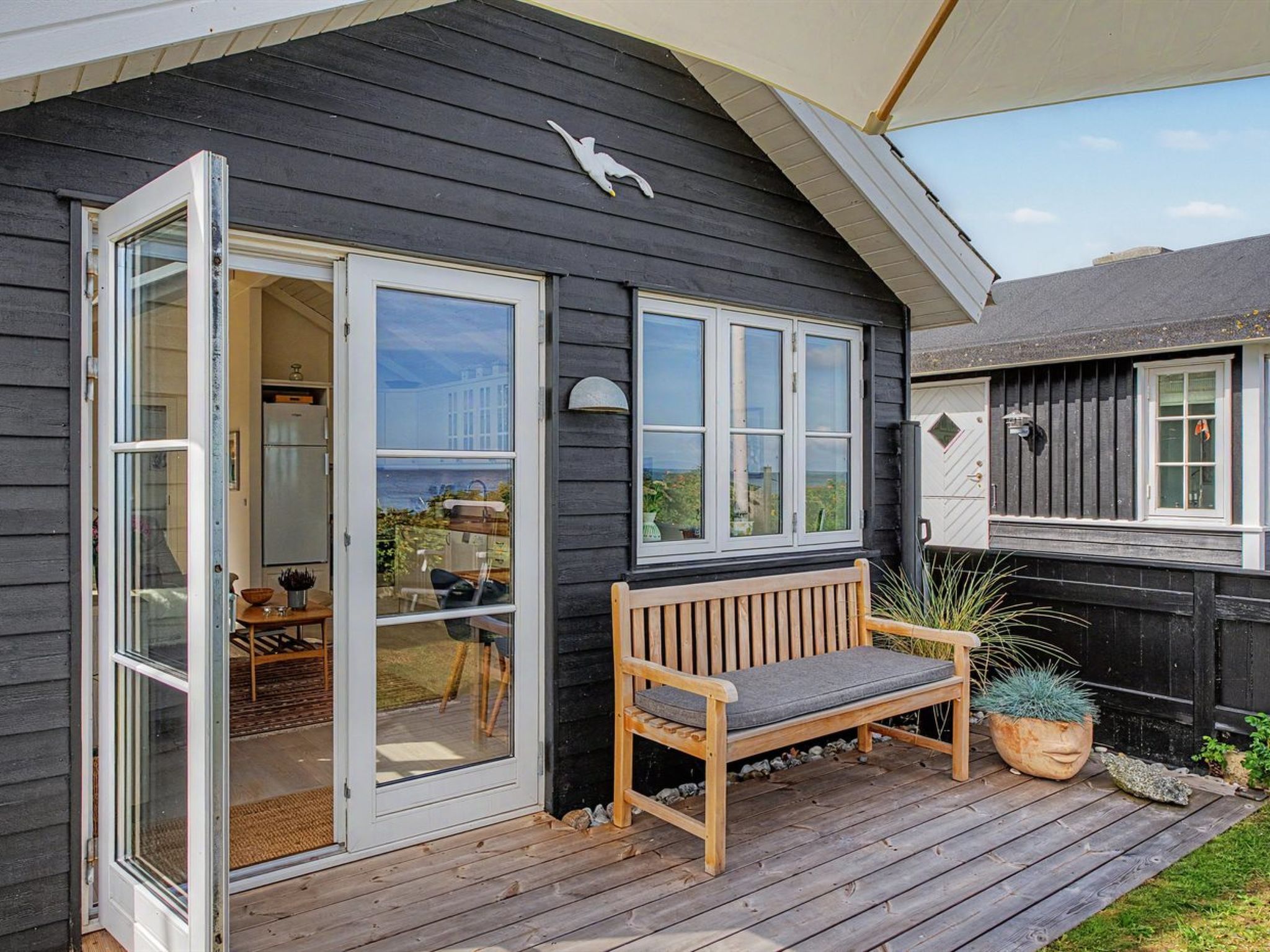 A wooden deck with a bench and a potted plant, a sliding glass door leading to a patio area, and a view of the sea.