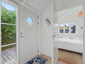Quarto com cama, porta com janela, pequena janela e quadro de um pássaro fixado na parede.