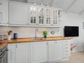 A modern kitchen with white cabinetry, a wooden countertop, a built-in dishwasher, and a flat-screen TV mounted on the wall. - "Joachim" - 10m from the sea by Interhome (Otterup)