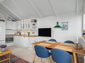 Cozinha moderna com armários brancos, área de jantar com cadeiras azuis e uma luminária pendente verde.