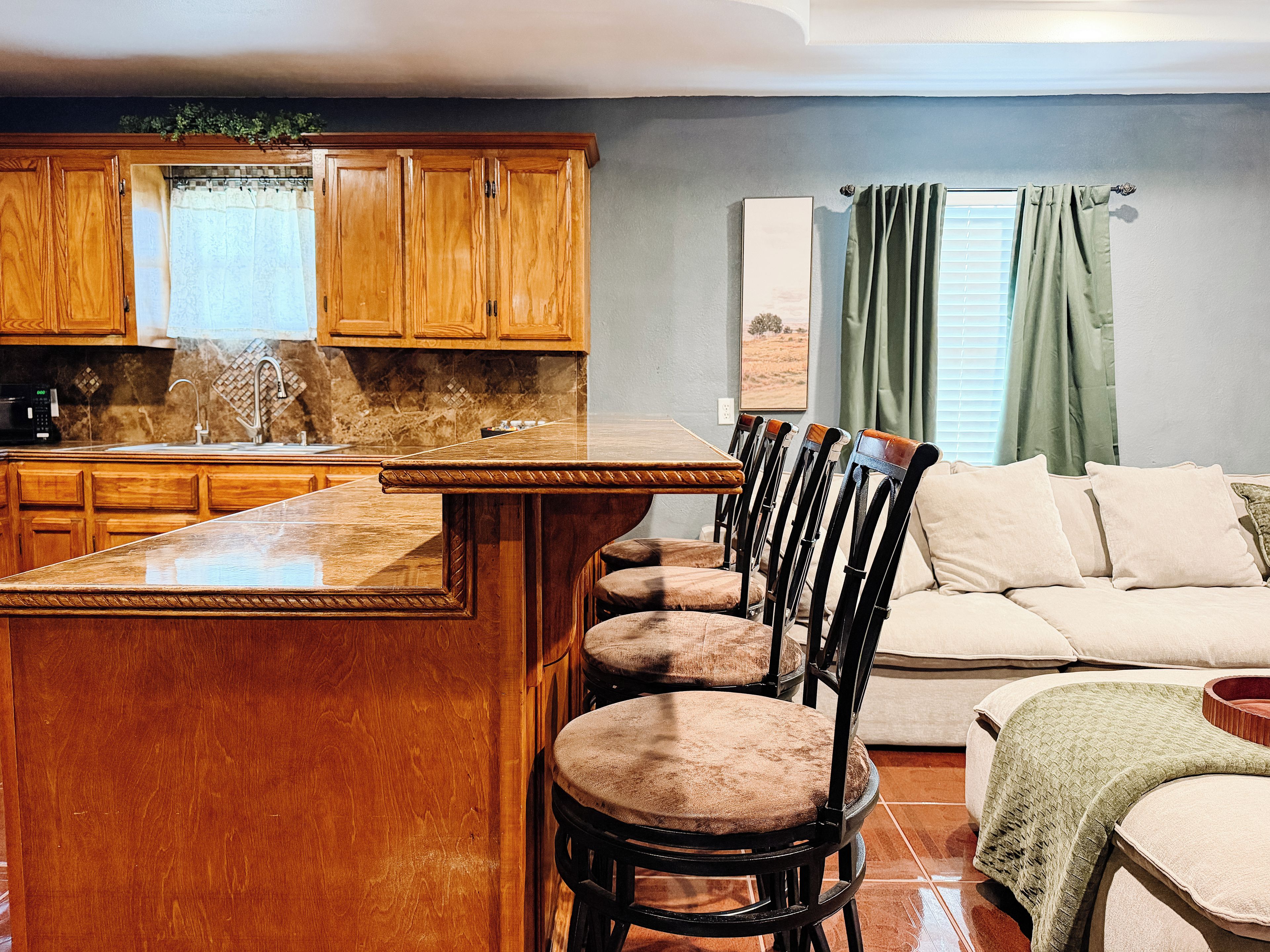 A kitchen with wooden cabinets, a bar area, and a dining space with chairs and a sofa.