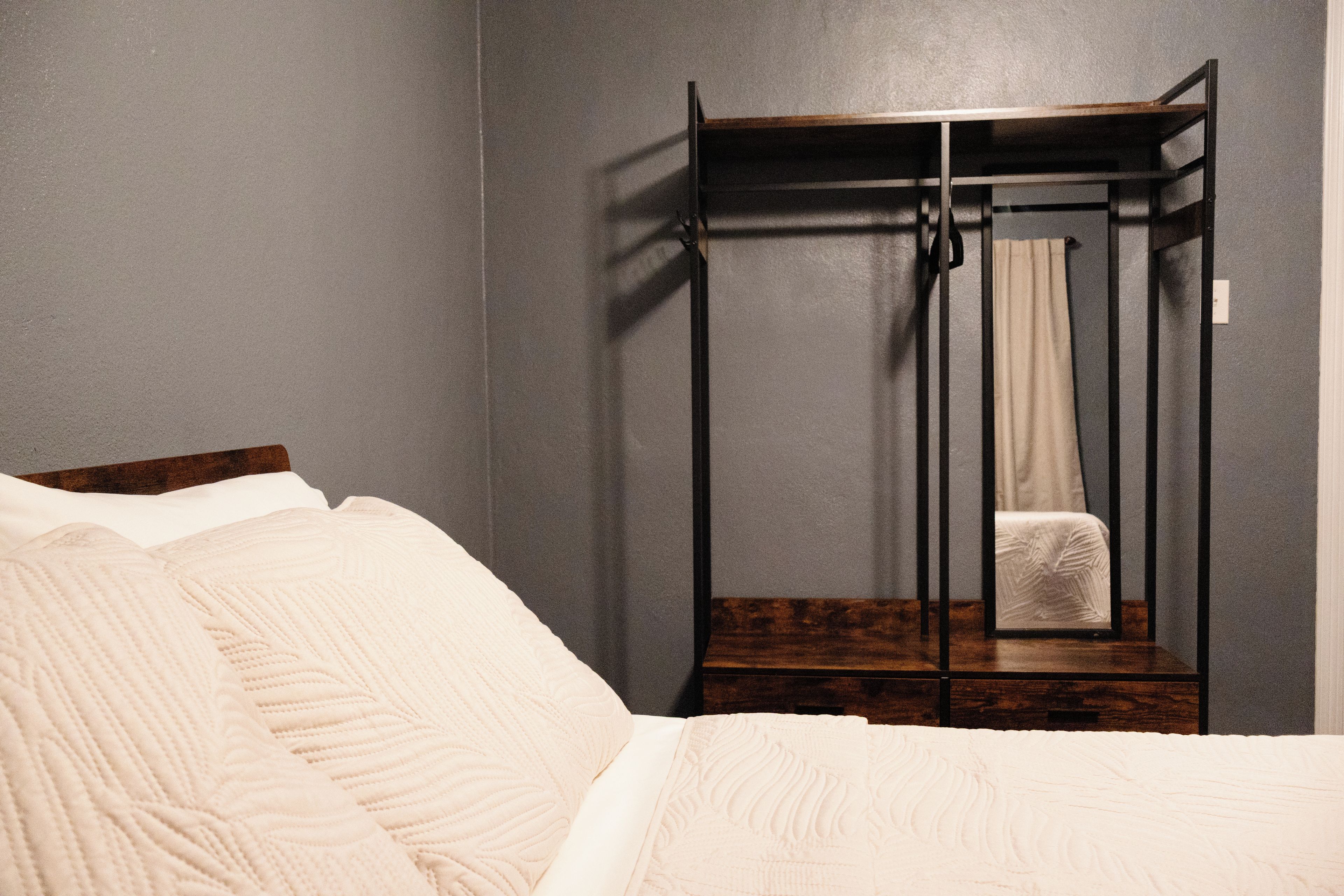 Een kamer met een bed, een houten hoofdbord, een kledingkast en een spiegel.