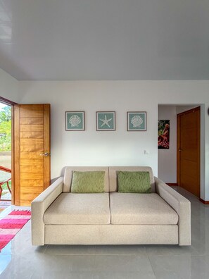 A neutral-toned sofa with two cushions, a wooden door, and three framed wall art pieces.