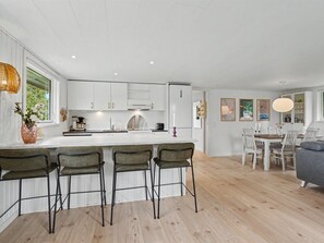 Een moderne keuken met witte kasten, een centraal keukenblok met barkrukken, en een eethoek met een tafel en stoelen.
