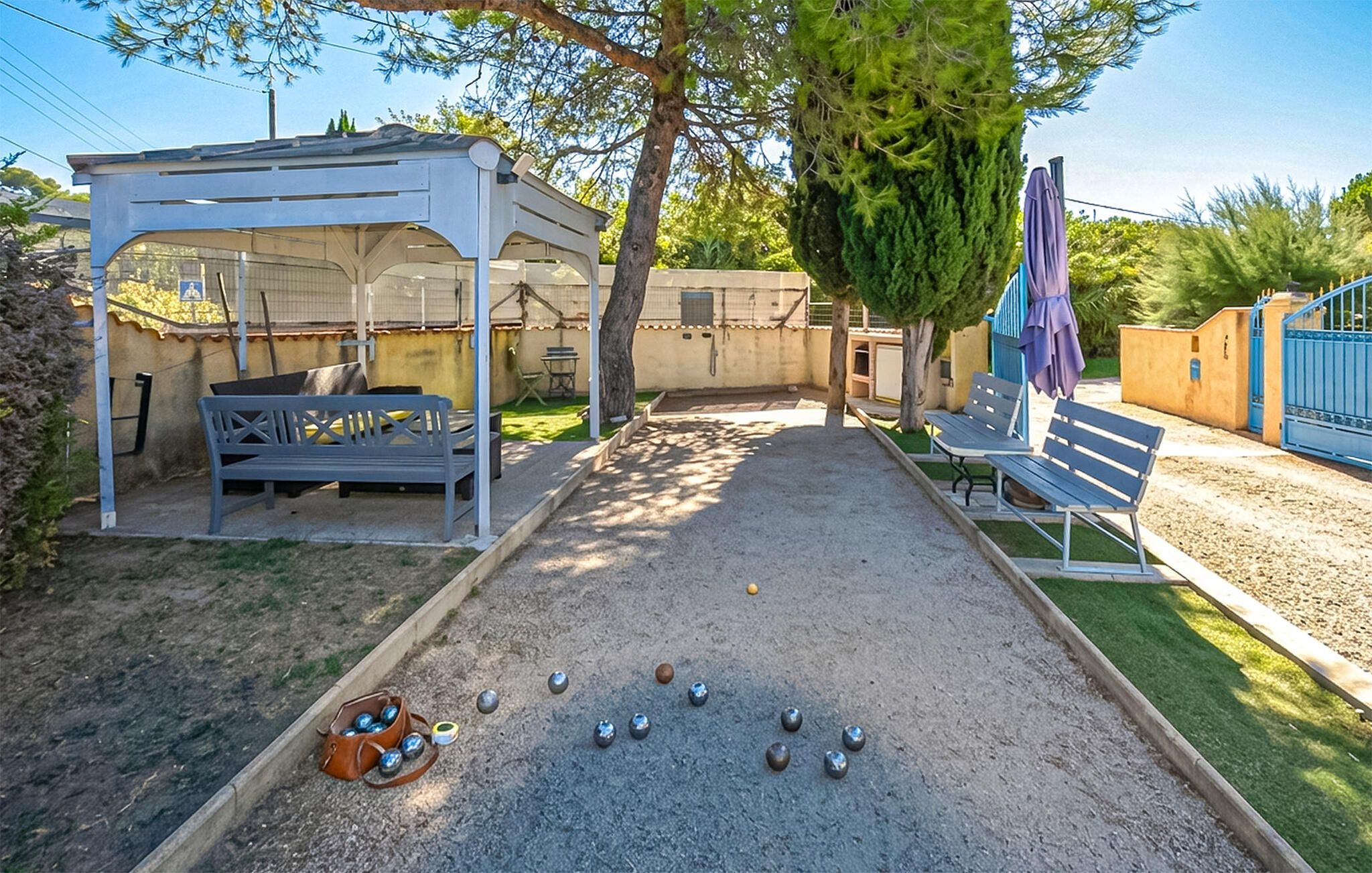 Une cour avec un espace de repos abrité, un terrain de pétanque et un portail bleu.