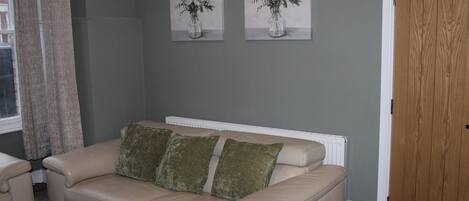 A living room with a beige sofa, two cushions, a radiator, and two wall-mounted paintings of flowers.