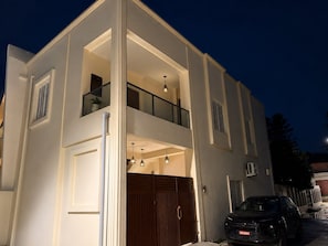 A two-story building with a balcony, a garage door, and a car parked in front.