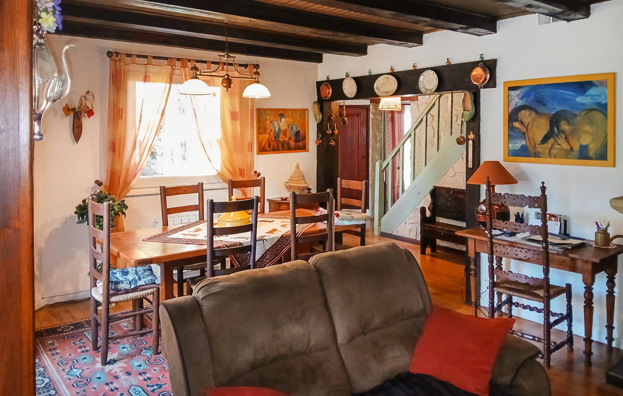 Un espace repas avec une table et des chaises en bois, un tapis à motifs et un escalier menant à un autre niveau.