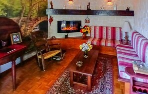 A cozy living room with a fireplace, a sofa, a chair, and a small table with flowers. - Maison de charme en campagne (Lanarce)