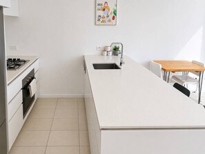 Eine moderne Küche mit weißer Arbeitsplatte, Edelstahlgeräten und einer kleinen Spüle.