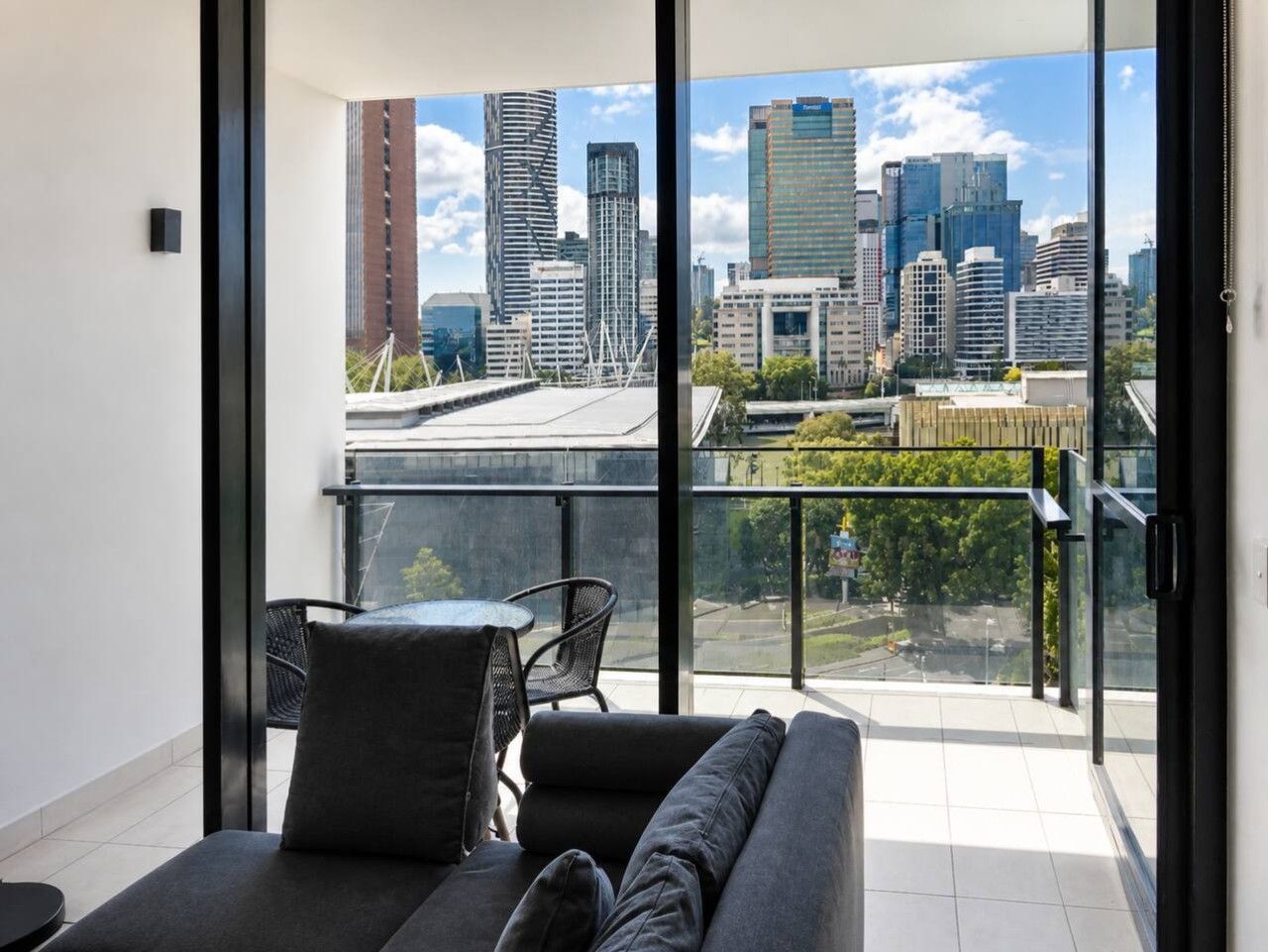 A modern balcony with a sofa and chairs, overlooking a cityscape with tall buildings.