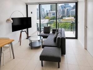 A modern living room with a sofa, a TV, a coffee table, and a dining table. - Brisbane City Views | 2BR Near South Bank & QPAC (South Brisbane)