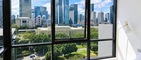 A hotel room with a large window offering a city skyline view.