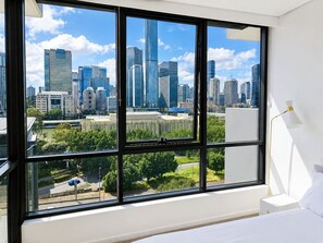 A hotel room with a large window offering a city skyline view. - Brisbane City Views | 2BR Near South Bank & QPAC (South Brisbane)