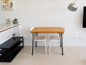 A modern kitchen with a wooden table, two white chairs, a black shelf, and a pendant light. - Brisbane City Views | 2BR Near South Bank & QPAC (South Brisbane)