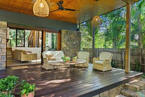Un patio al aire libre con mobiliario de mimbre, un ventilador de techo y una pared de piedra.