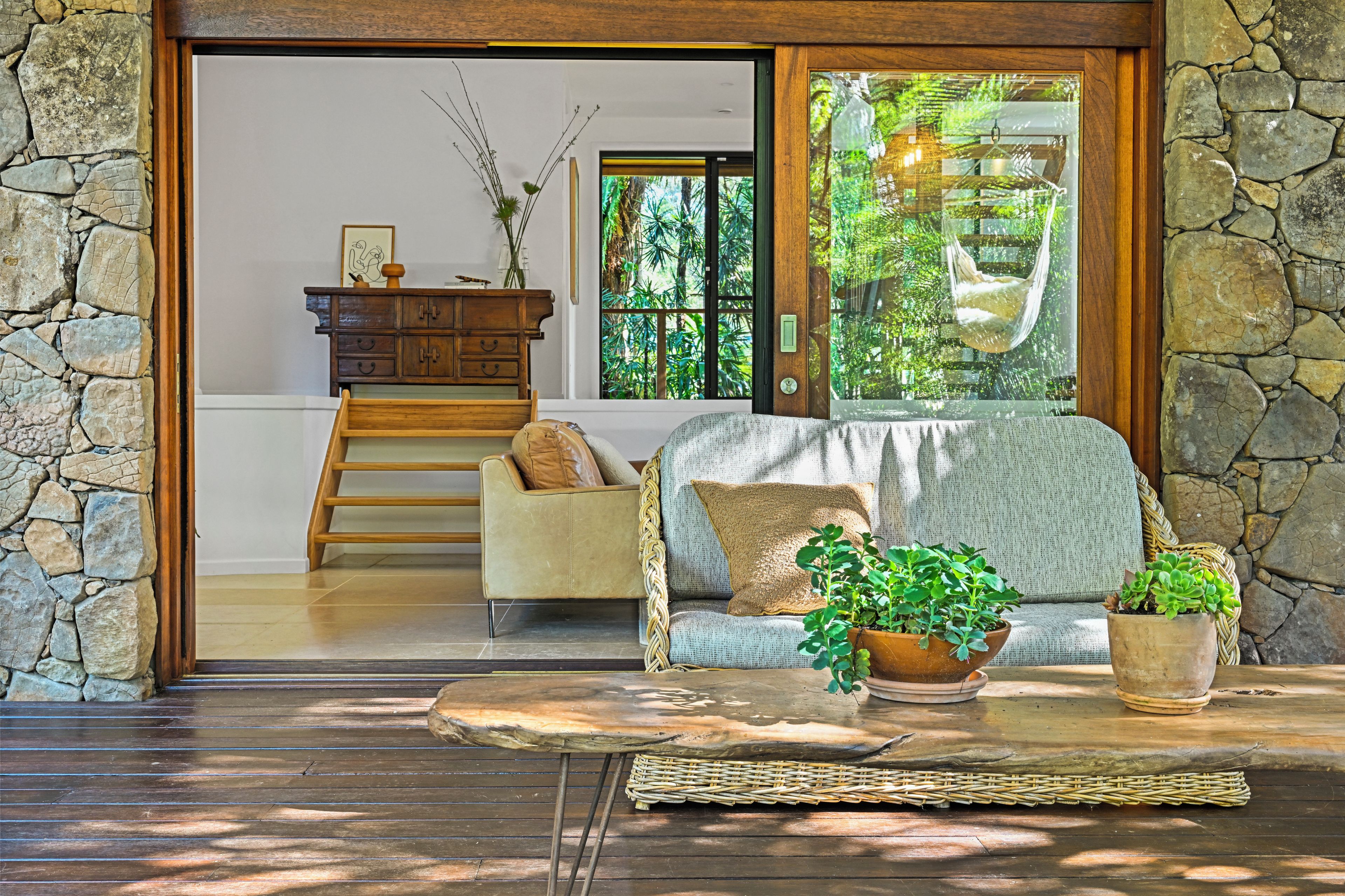 A cozy living room with a stone wall, a wooden bench, a sofa with cushions, and a potted plant.