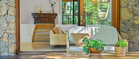 A cozy living room with a stone wall, a wooden bench, a sofa with cushions, and a potted plant.