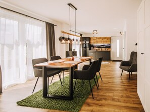A modern kitchen with wooden cabinets, a dining area with a wooden table and black chairs, and a green rug on the floor. - Chalet at Mollcesine (Oderwitz)