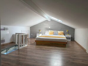 Ein Schlafzimmer mit schrägverlaufender Decke, einem Bett mit Kissen, einem Nachttisch und einem Spiegel.