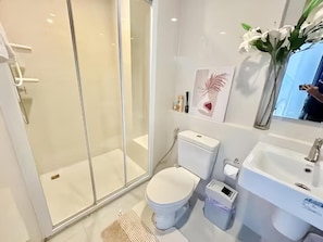 A modern bathroom with a glass-enclosed shower, a toilet, a sink, and a mirror. - The Base Central Pattaya (Muang Pattaya)
