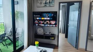 Een moderne woonkamer met een glazen wand, een flatscreen televisie, een witte tafel en een bloemenvaas.