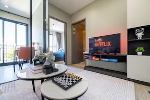 A modern living room with a flat-screen TV displaying 'NETFLIX,' a chessboard on a table, and a sofa with a decorative statue. - The Base Central Pattaya (Muang Pattaya)