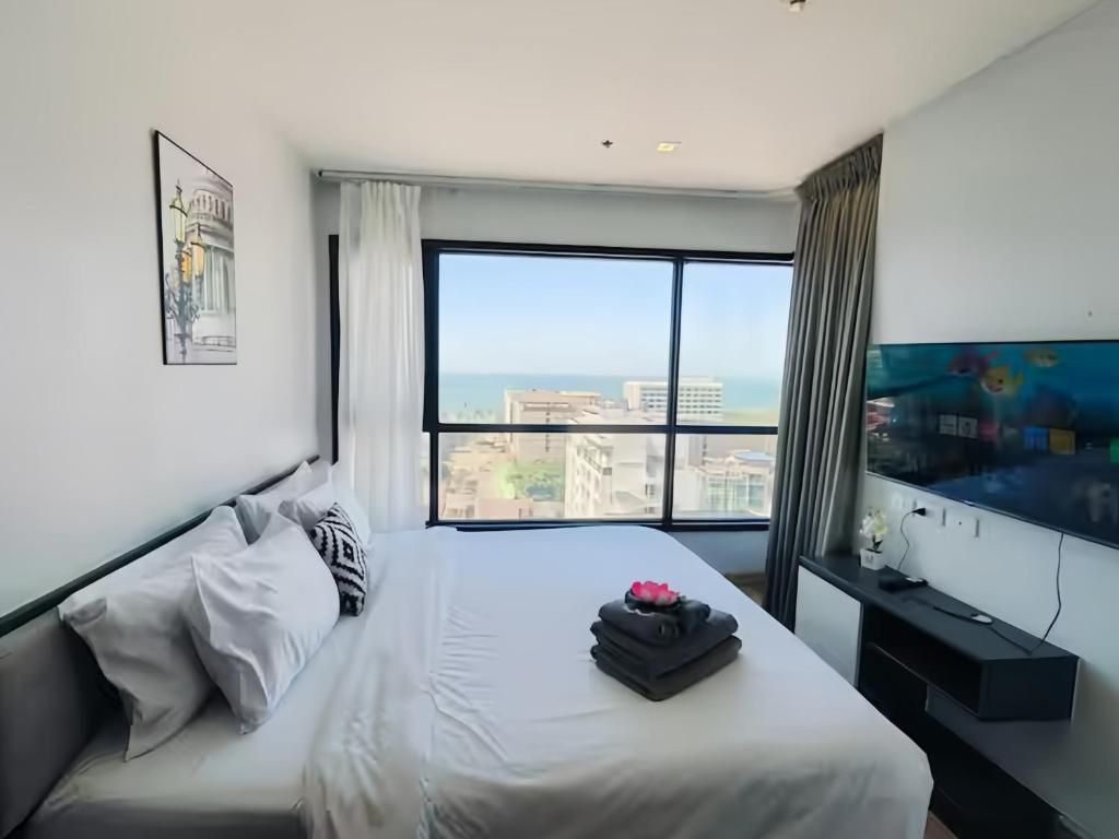 Habitación de hotel con un ventanal grande, una cama con ropa blanca, un televisor de pantalla plana y un cuadro en la pared.
