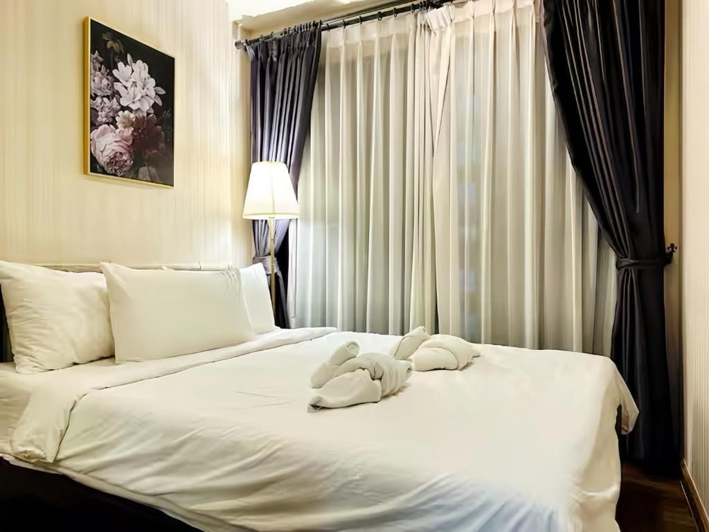 Une chambre d’hôtel avec un lit, des oreillers, une lampe et des rideaux.