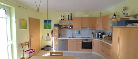 A kitchen with wooden cabinets, a dining table, chairs, a hanging light fixture, and a window.