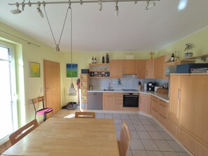 A kitchen with wooden cabinets, a dining table, chairs, a hanging light fixture, and a window.