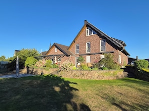A two-story brick house with a sloped roof, a stone wall, and a well-maintained lawn.