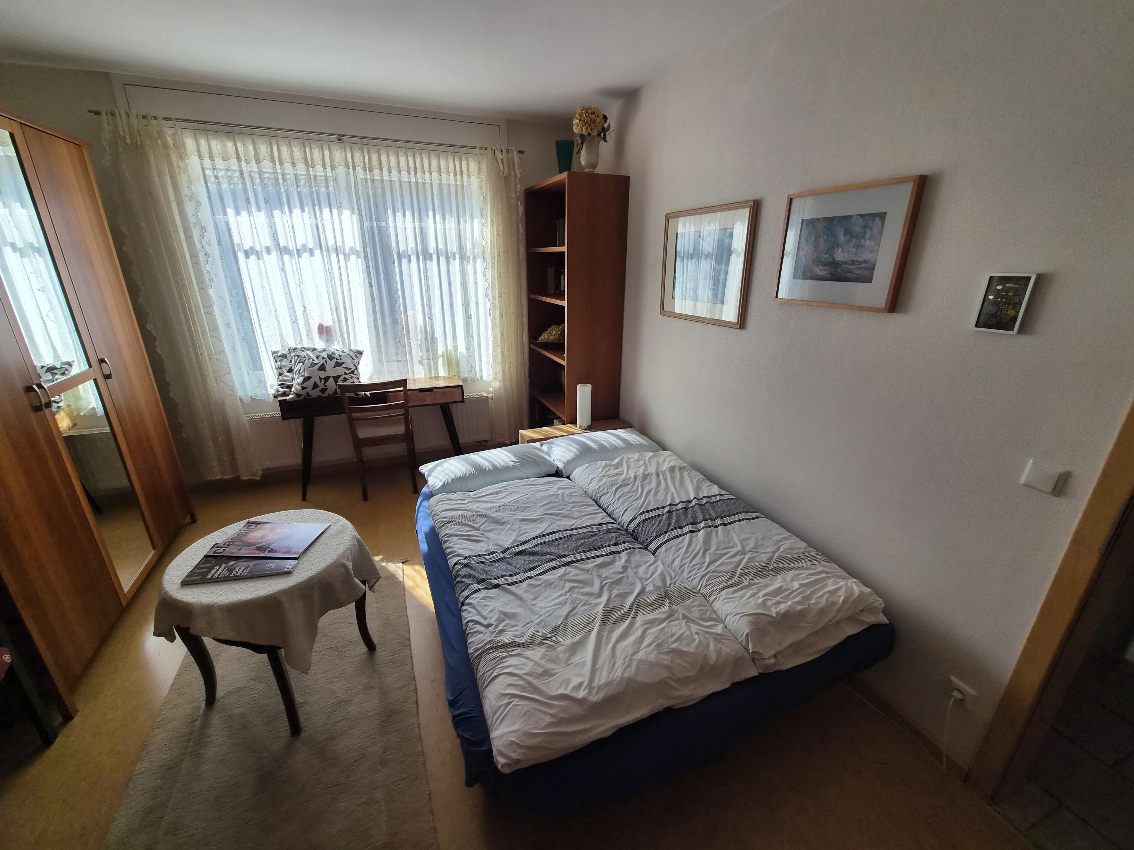 A bedroom with a bed, a desk, a chair, a bookshelf, and a window with curtains.