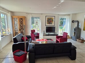 A modern living room with a black sofa, red chairs, a glass coffee table, and a TV.