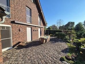 A brick building with a covered patio area, outdoor seating, and a garden.