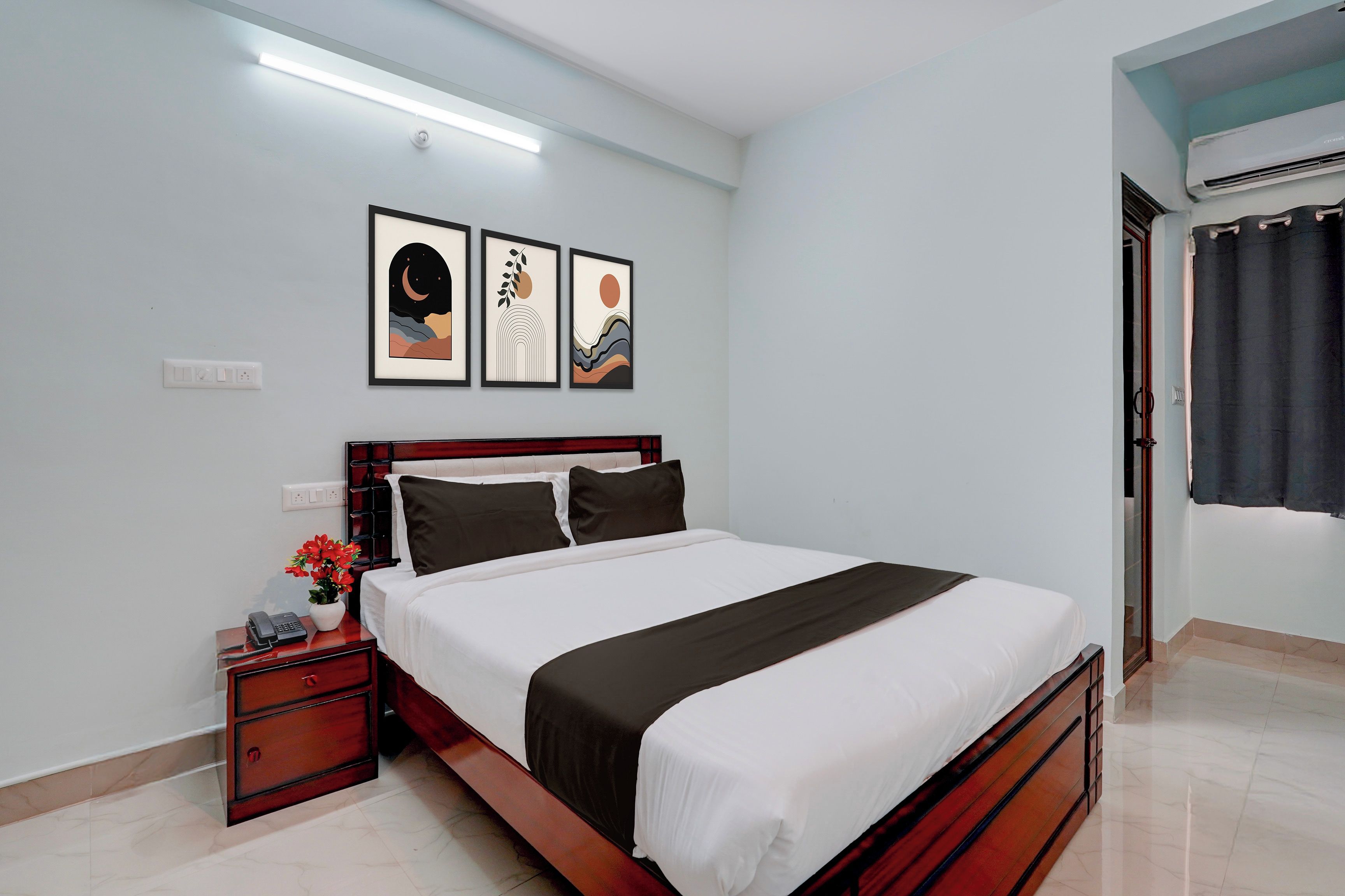 Un dormitorio con cama, mesitas de noche, aire acondicionado de pared y cuadros enmarcados.