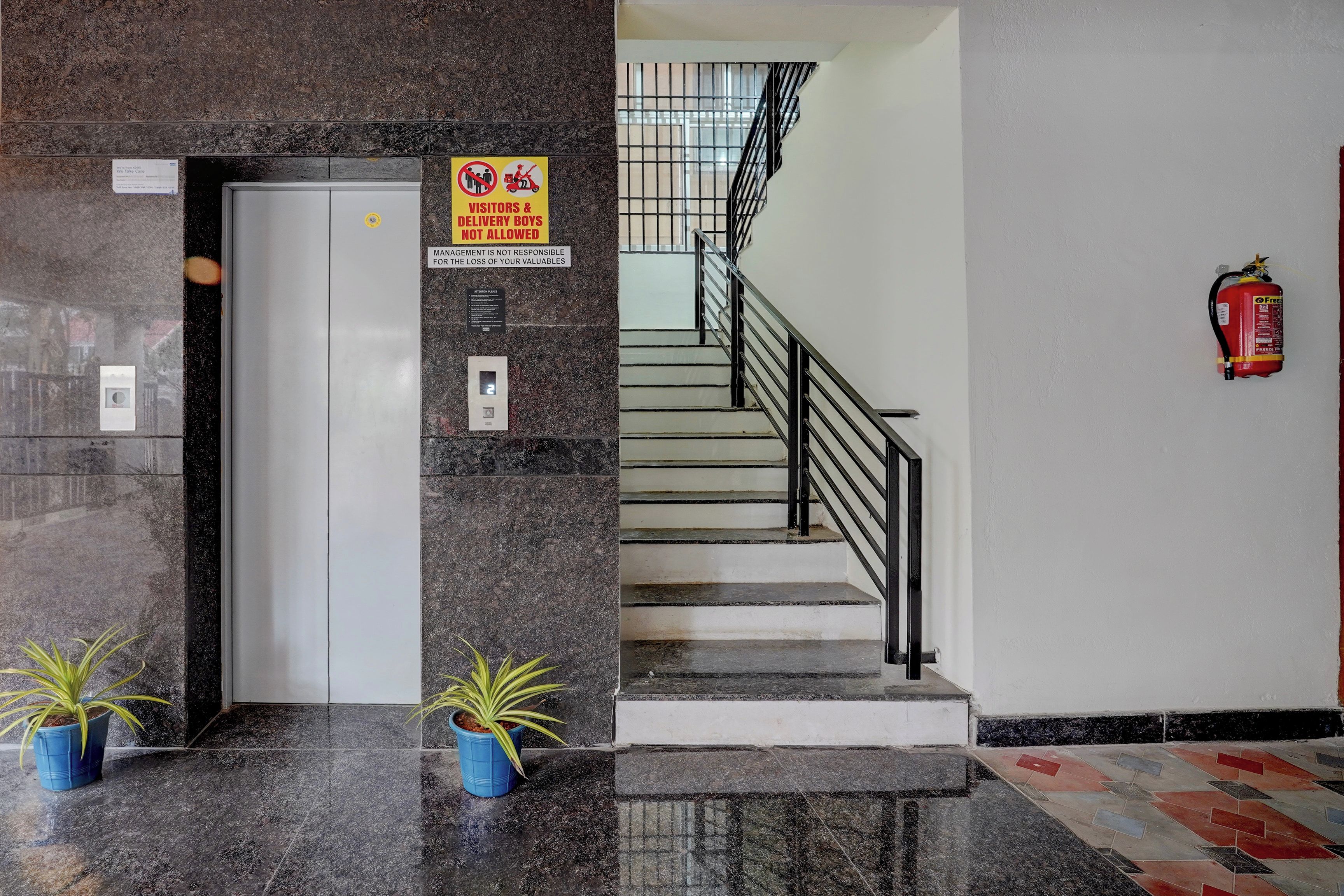 Zona de recepción de un hotel con mostrador de mármol, extintor y escalera.