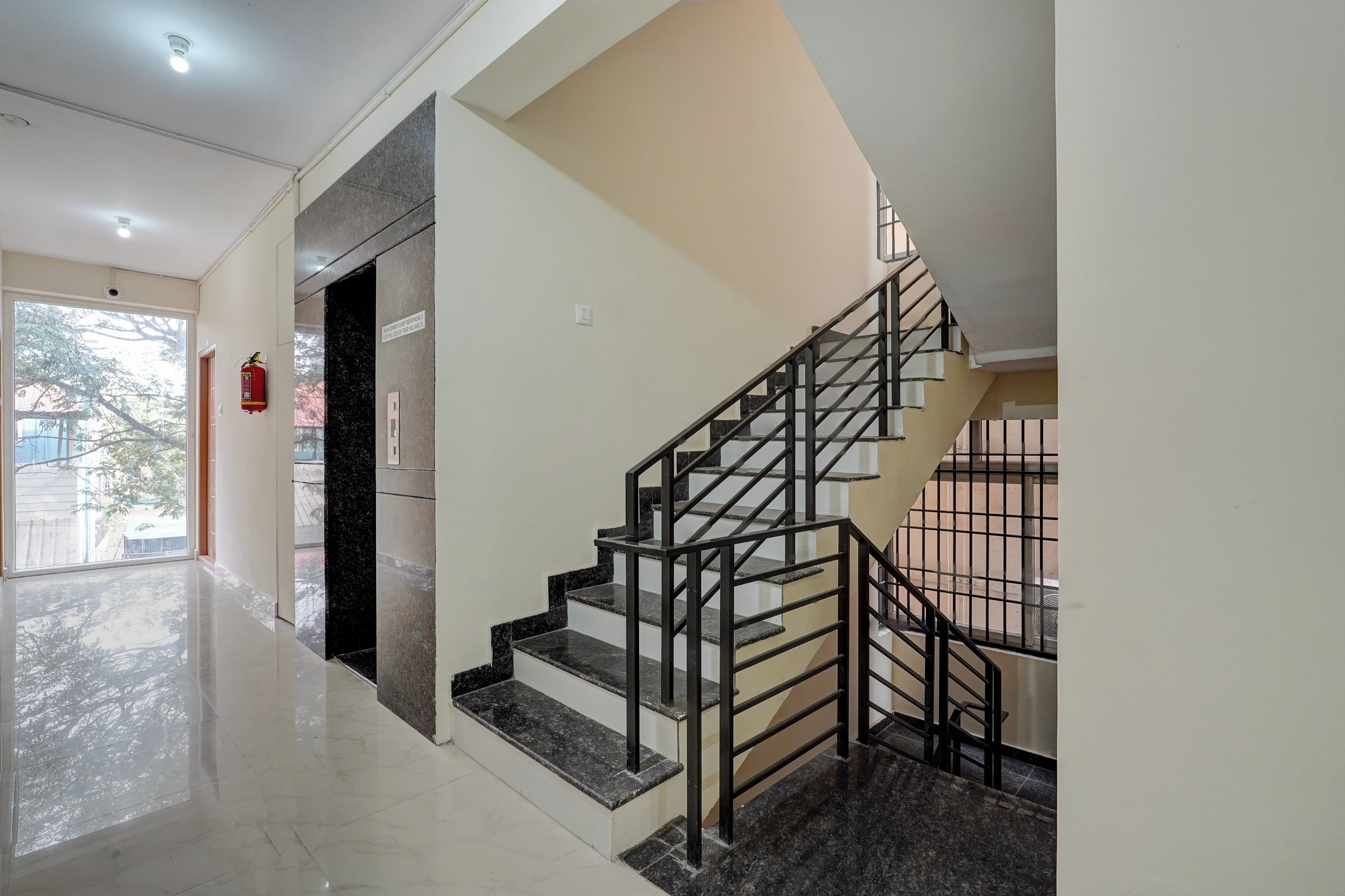 A staircase with a metal railing, a fire extinguisher mounted on the wall, and a door leading to an outdoor area.