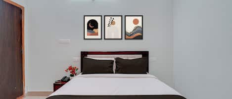 A hotel room with a bed, a nightstand, a phone, and a wall with three framed pictures.