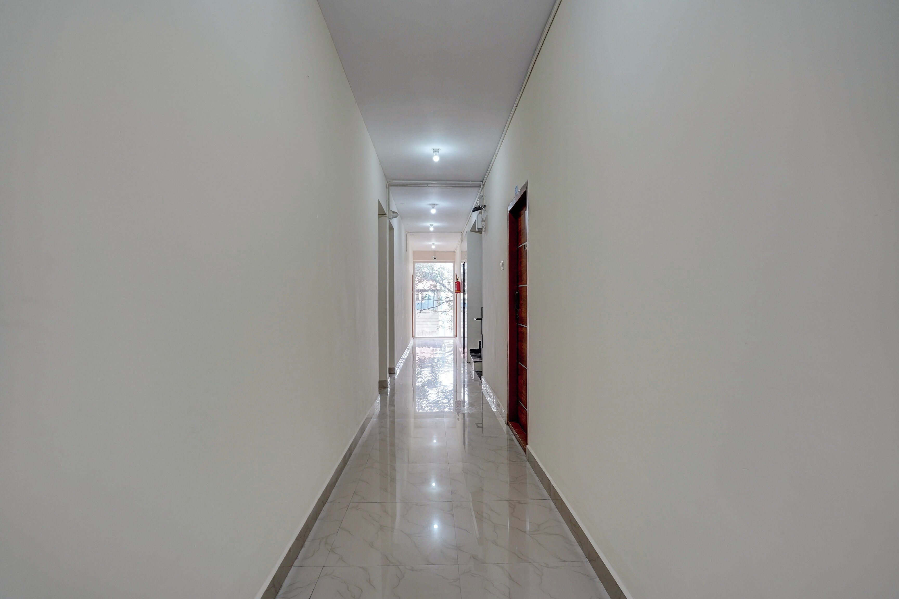 Un pasillo con piso de baldosas, paredes blancas y una puerta a la derecha.