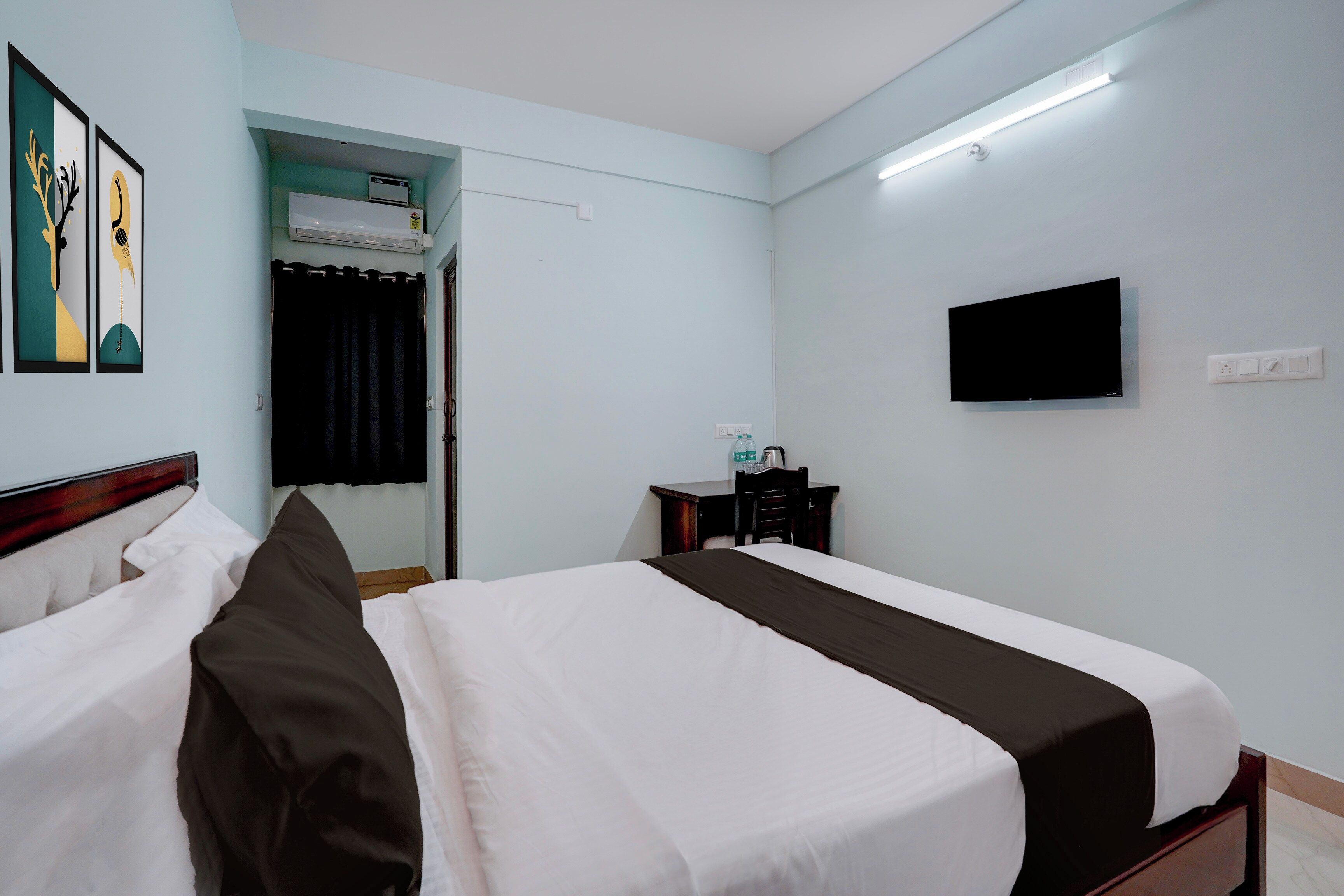 A hotel room with a bed, a television, a desk with a chair, and a window with curtains.