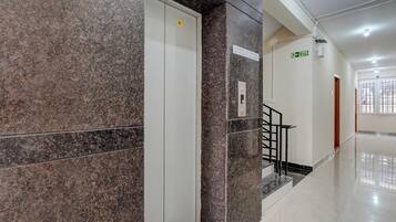 A clean, modern hallway with a marble wall, a white elevator, and a fire exit sign.