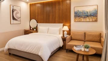 Habitación de hotel con una cama grande, un sofá, una mesa redonda, una mesita de noche, una lámpara, un espejo y dos cuadros en las paredes.
