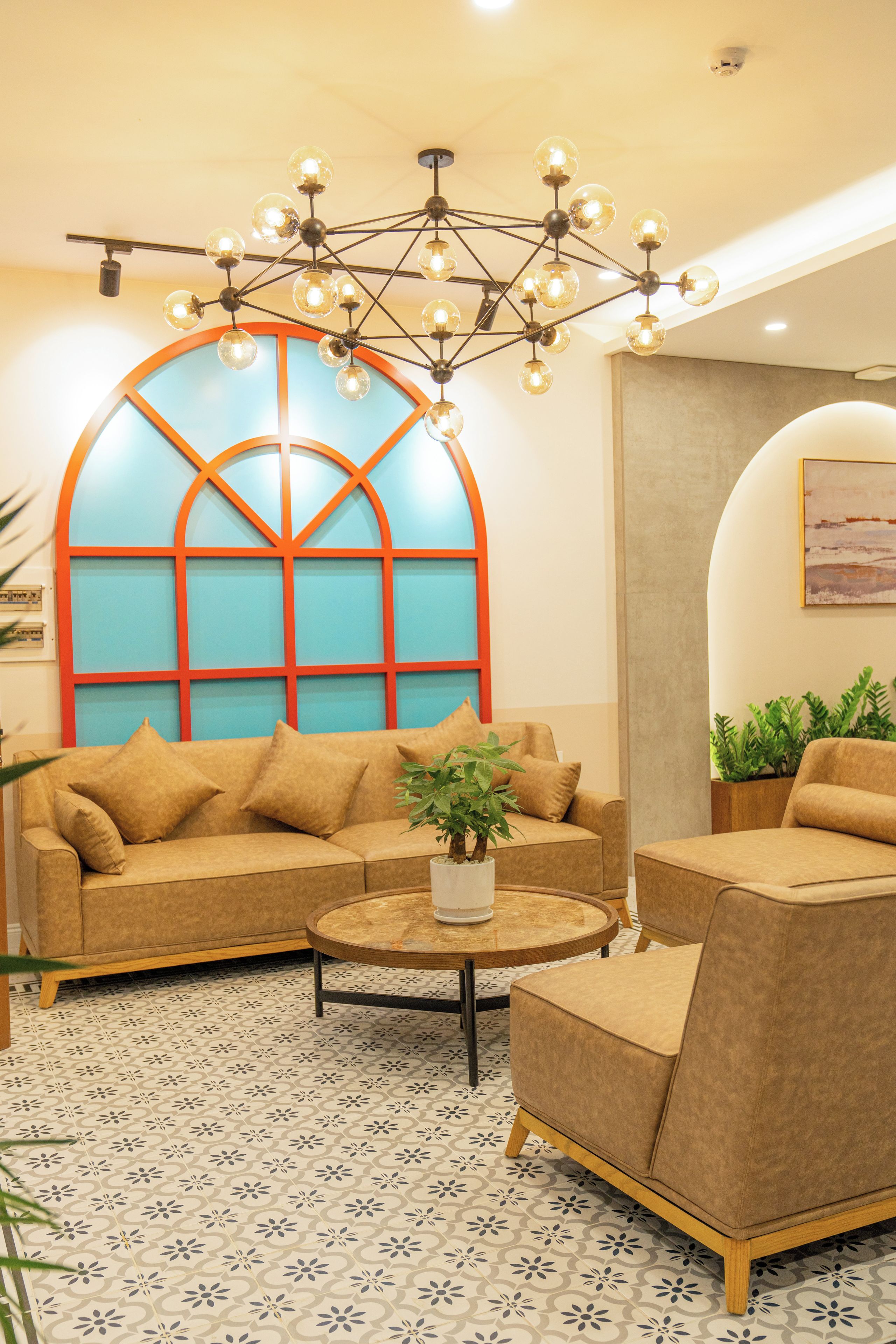 Una sala de estar moderna con un sofá, un sillón y una mesa de centro. Cuenta con un ventanal de diseño geométrico y una lámpara de techo.
