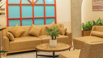 Una sala de estar moderna con un sofá, un sillón y una mesa de centro. Cuenta con un ventanal de diseño geométrico y una lámpara de techo.