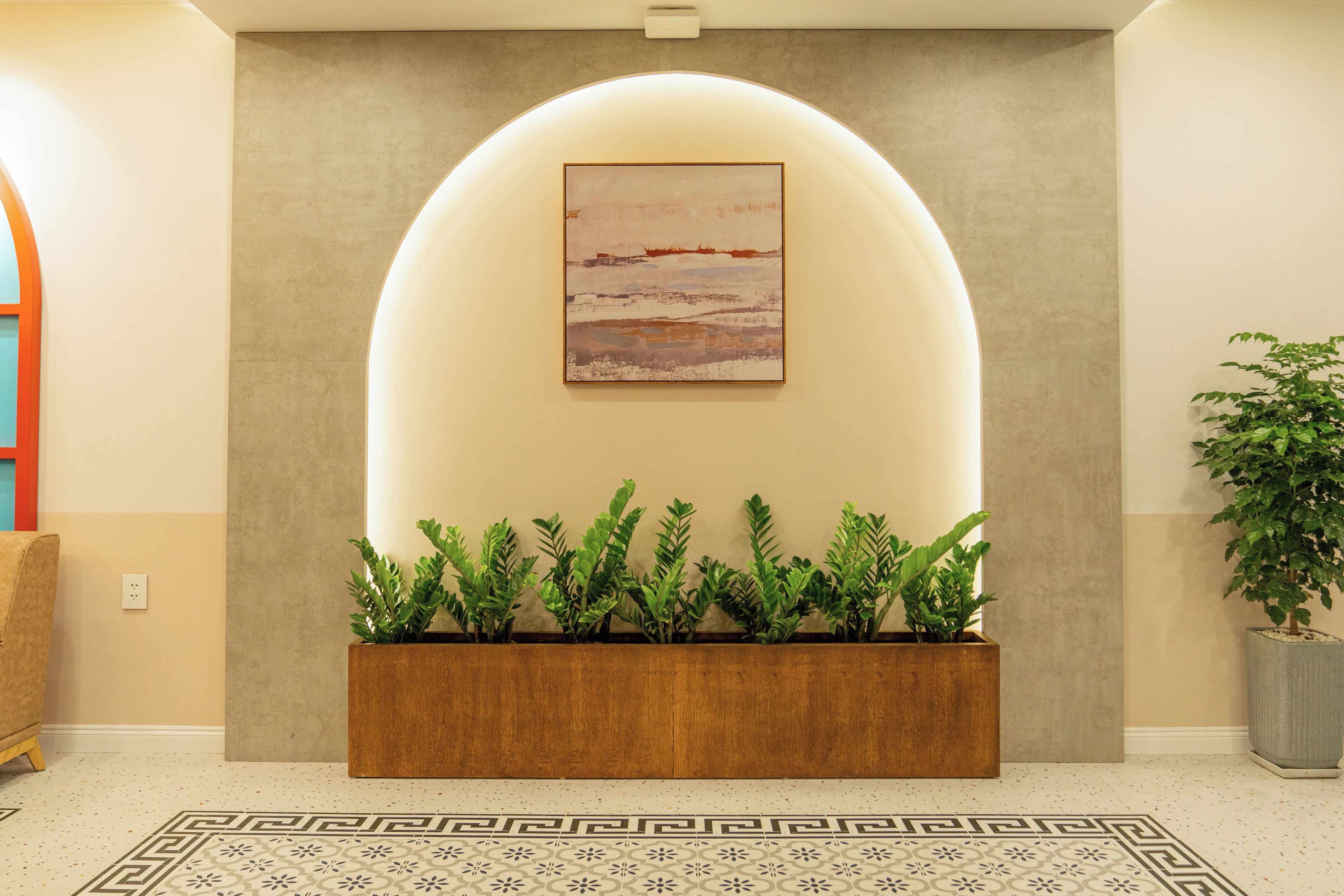 Un área de recepción de diseño moderno, con una jardinera de madera con plantas verdes, una gran obra de arte enmarcada arriba y un suelo con estampado.
