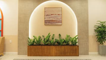 Un área de recepción de diseño moderno, con una jardinera de madera con plantas verdes, una gran obra de arte enmarcada arriba y un suelo con estampado.