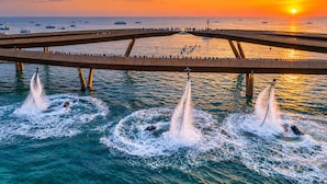Uma ponte sobre a água, com vários barcos e jatos aquáticos criando ondulações.